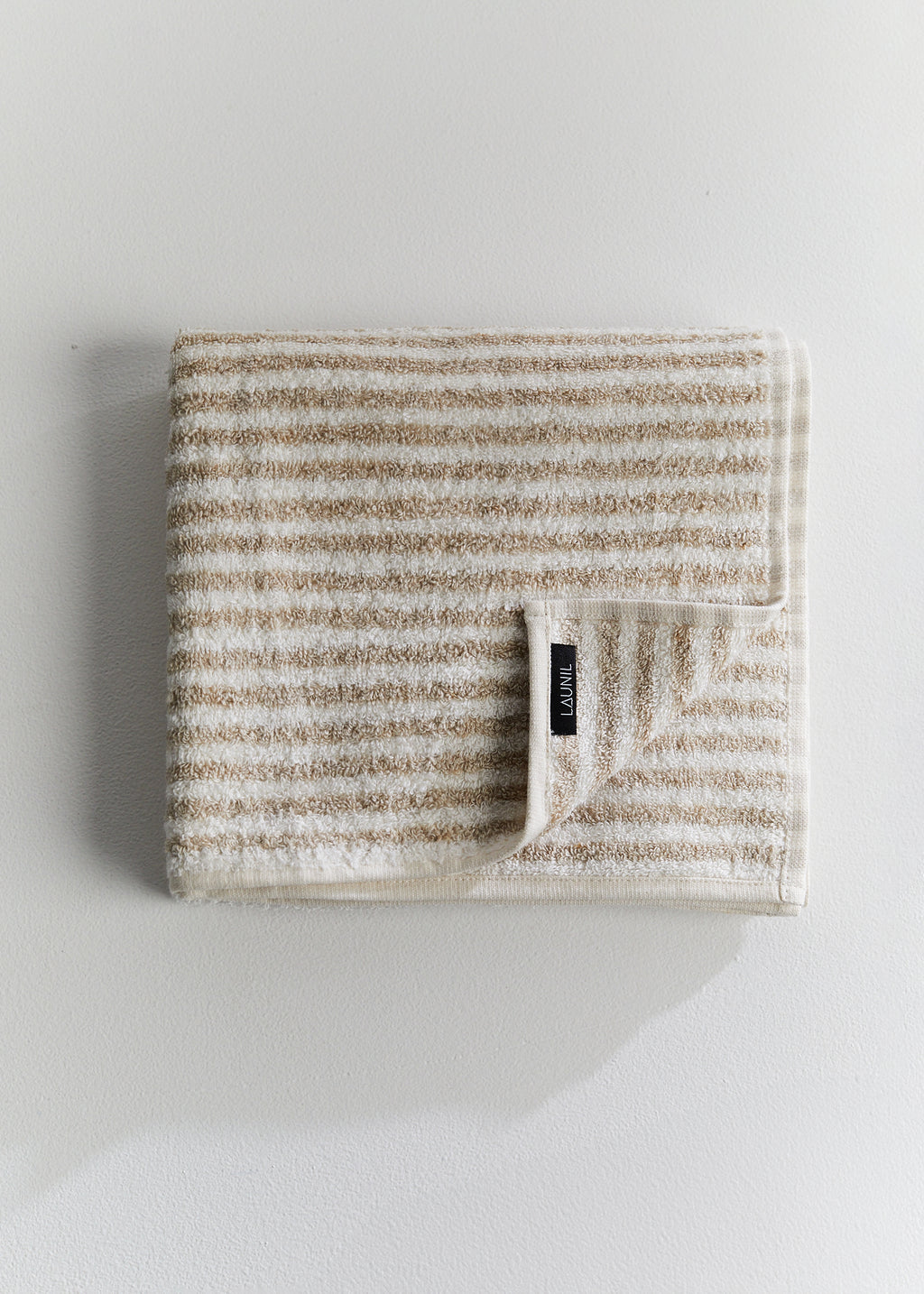 Folded beige and white striped linen terry towel with a LAUNIL label on a plain light background.