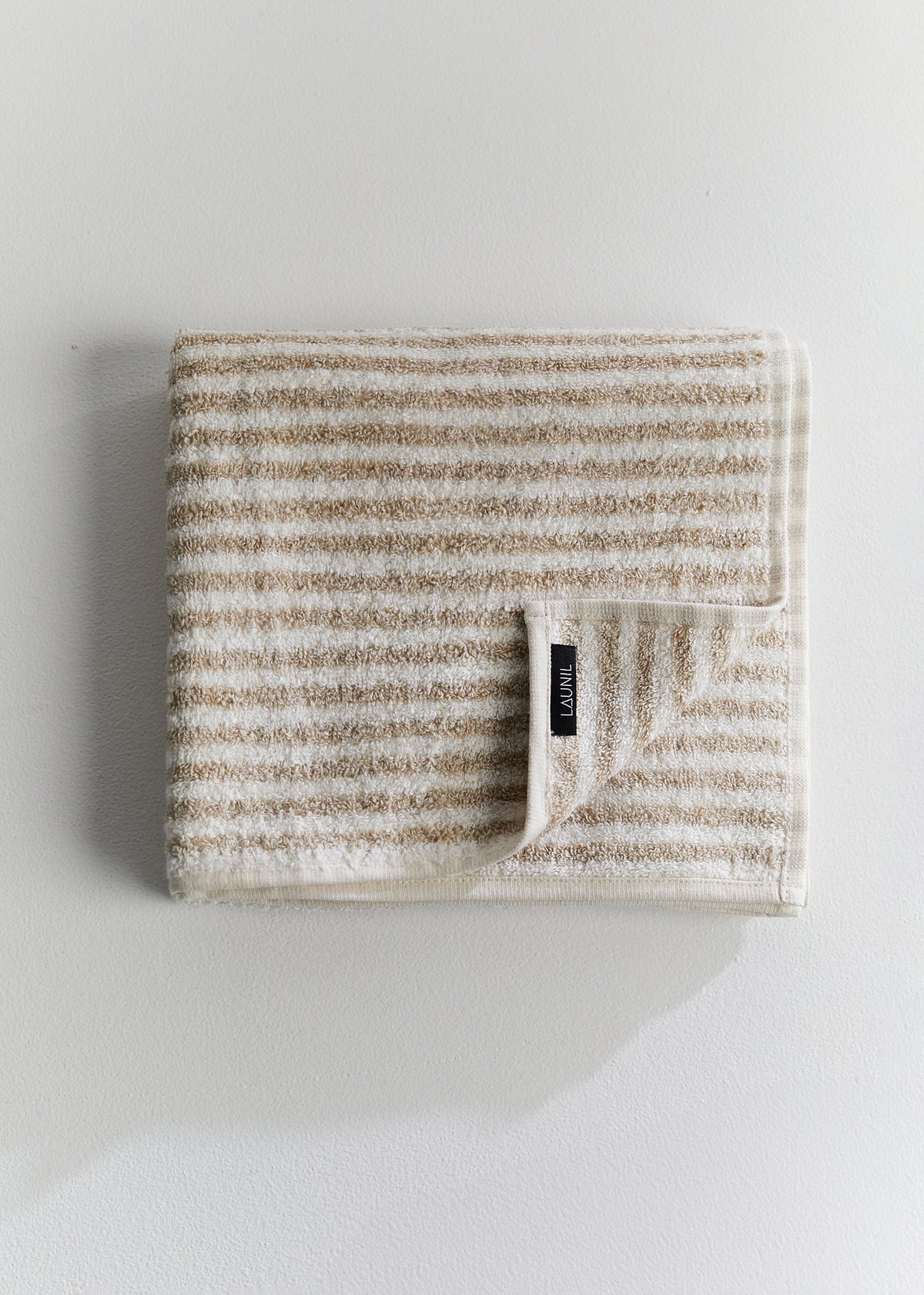 Folded beige and white striped linen terry towel with a LAUNIL label on a plain light background.