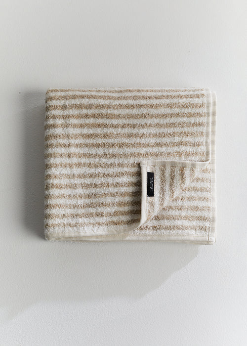 Folded beige and white striped linen terry towel with a LAUNIL label on a plain light background.