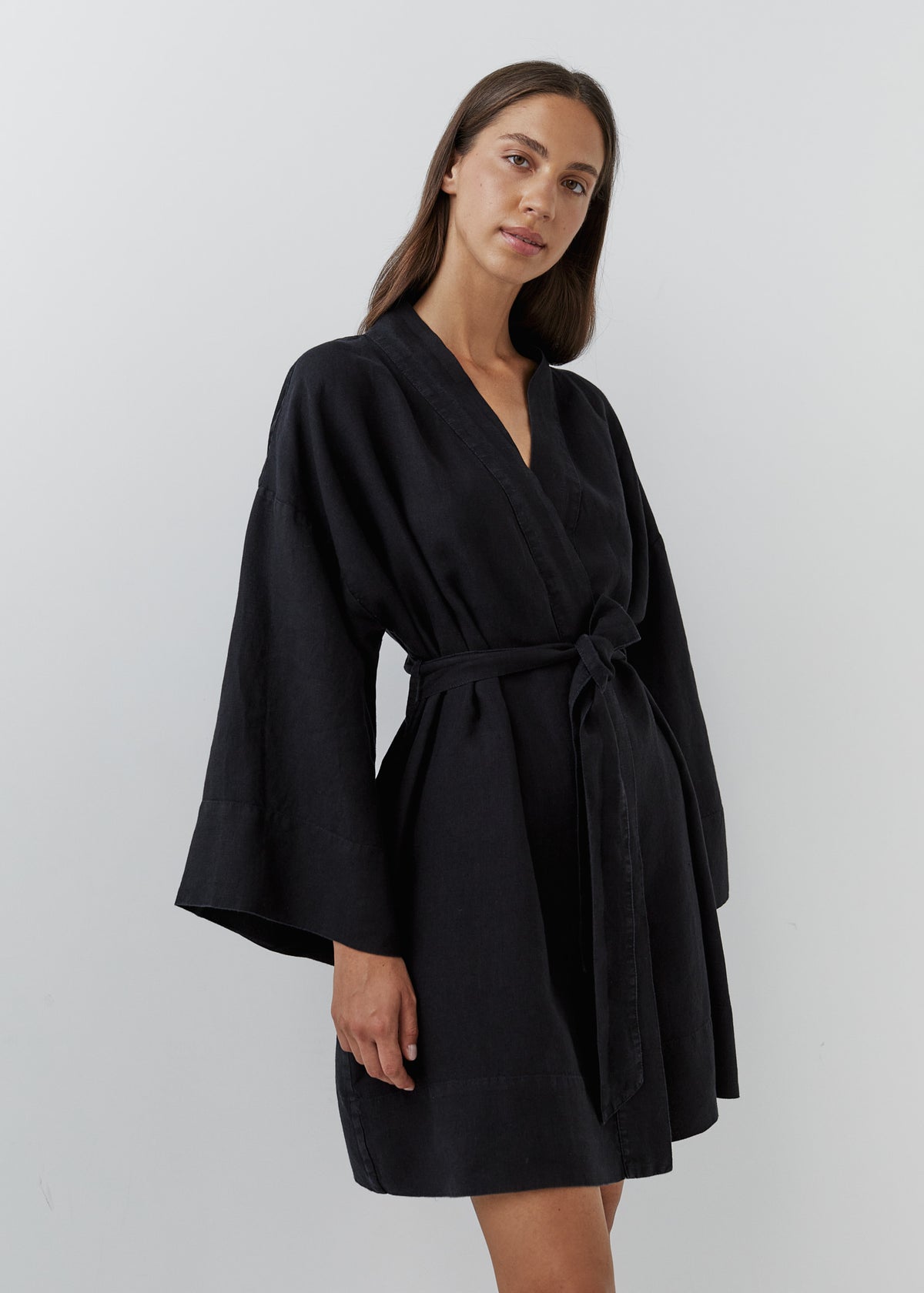 A woman wearing a short black linen robe with wide sleeves and an adjustable waist belt, shown from the front.
