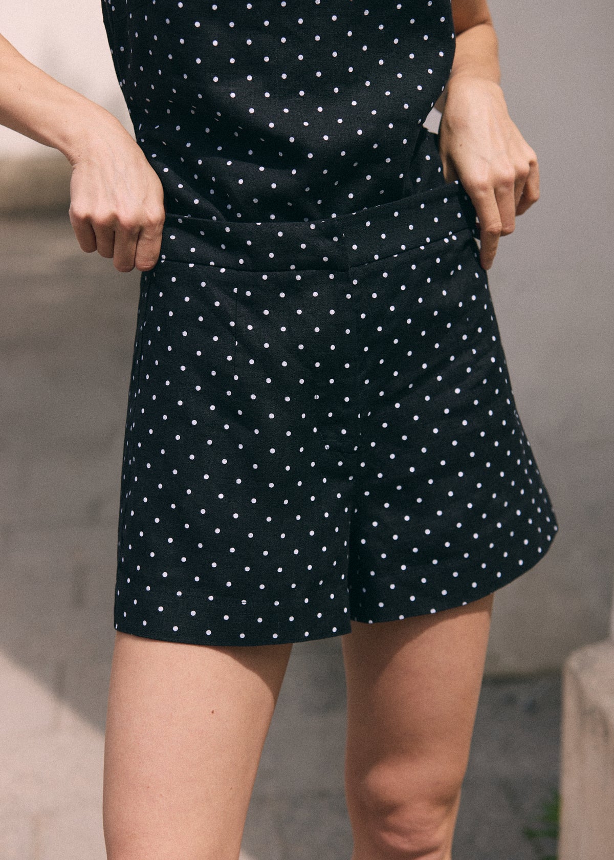 A close-up of a person wearing black shorts with a white polka dot pattern, holding the sides of the shorts to show their shape and fit.