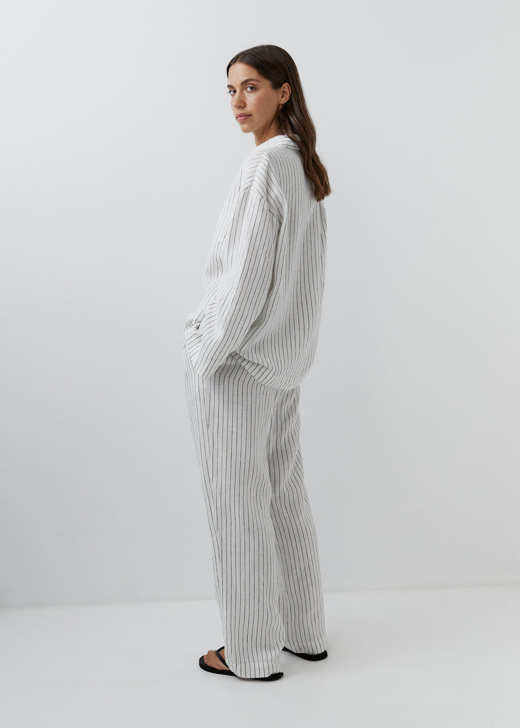 Woman wearing relaxed striped linen trousers with a matching button-down shirt.