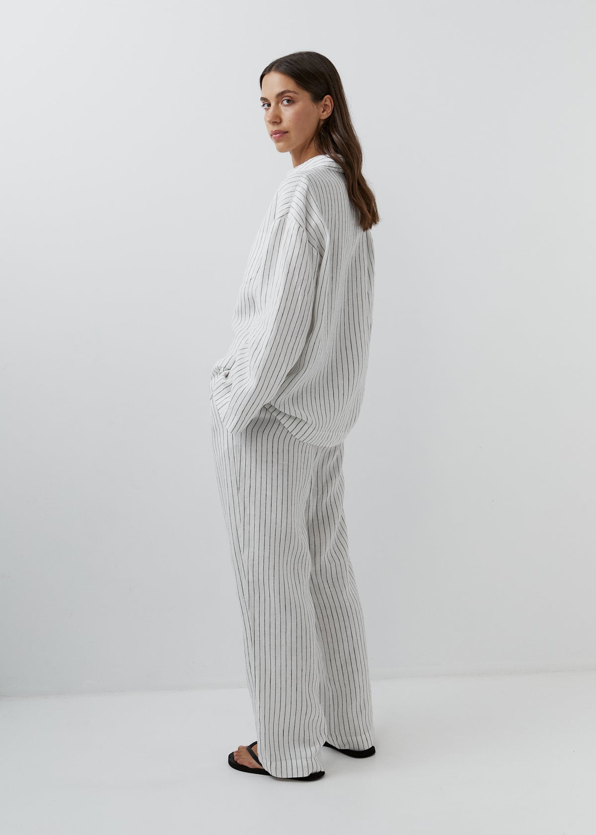 Woman wearing relaxed striped linen trousers with a matching button-down shirt.
