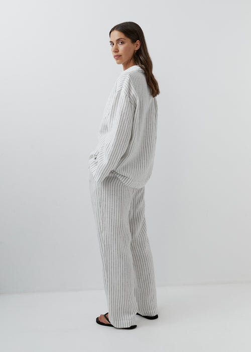Woman wearing relaxed striped linen trousers with a matching button-down shirt.