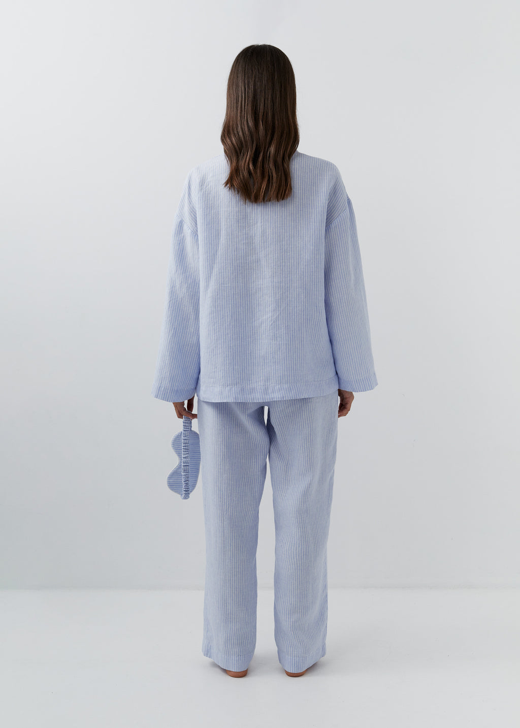 Back view of a woman wearing fine blue and white striped linen trousers with a relaxed straight-leg fit.