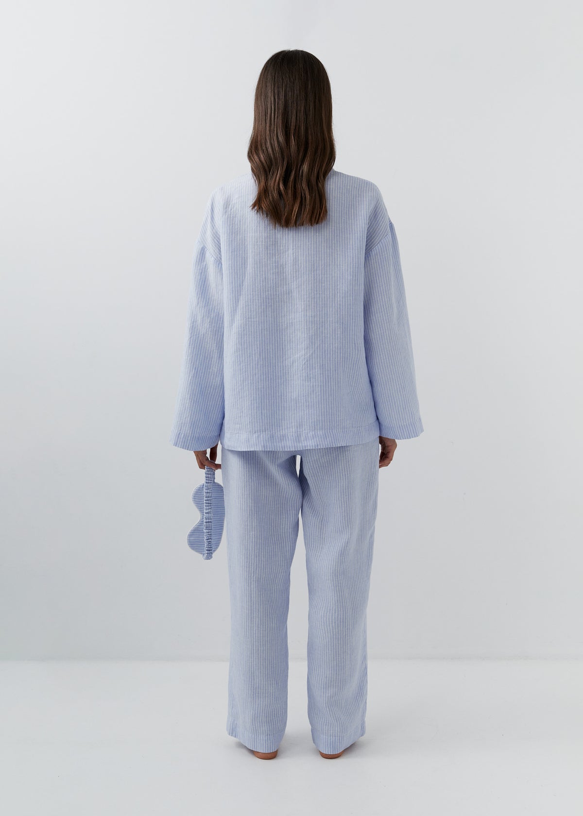 Back view of a woman wearing fine blue and white striped linen trousers with a relaxed straight-leg fit.