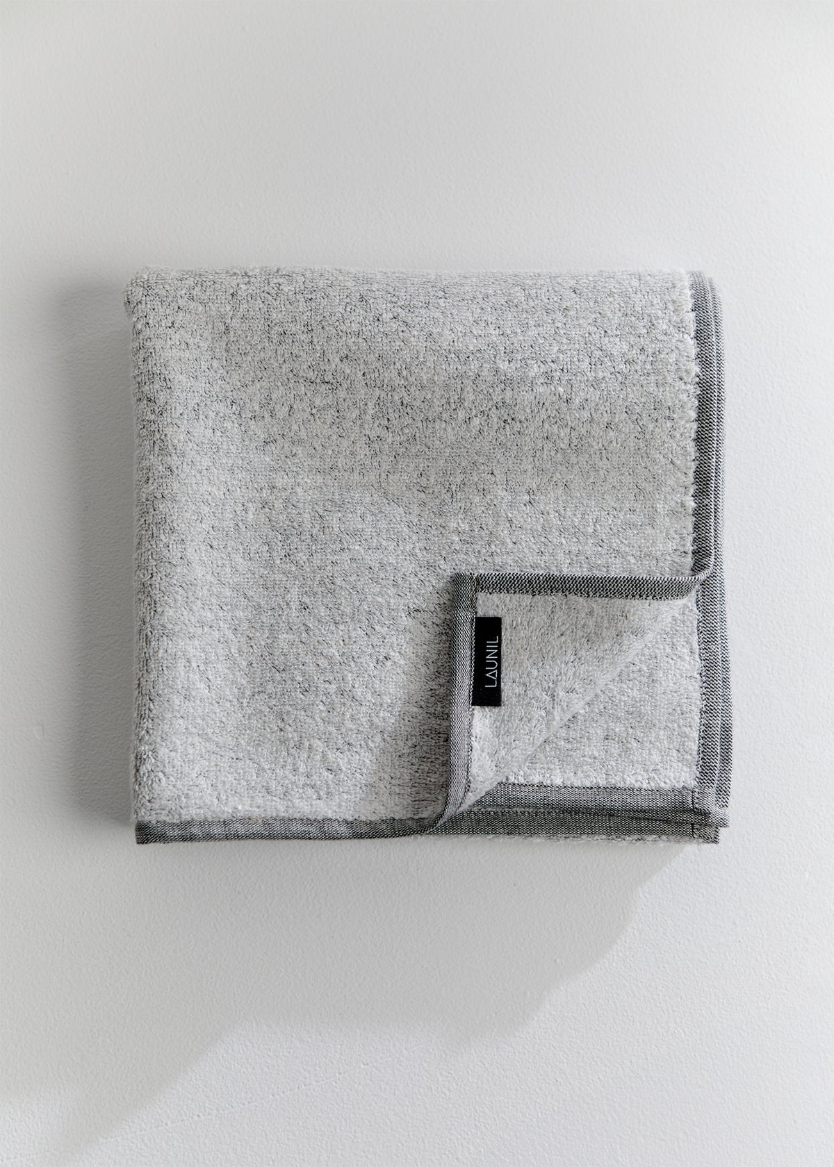 Folded grey terry towel made with 100% linen loops and a 100% cotton base, finished with dark grey edging and a LAUNIL label, photographed against a white background.