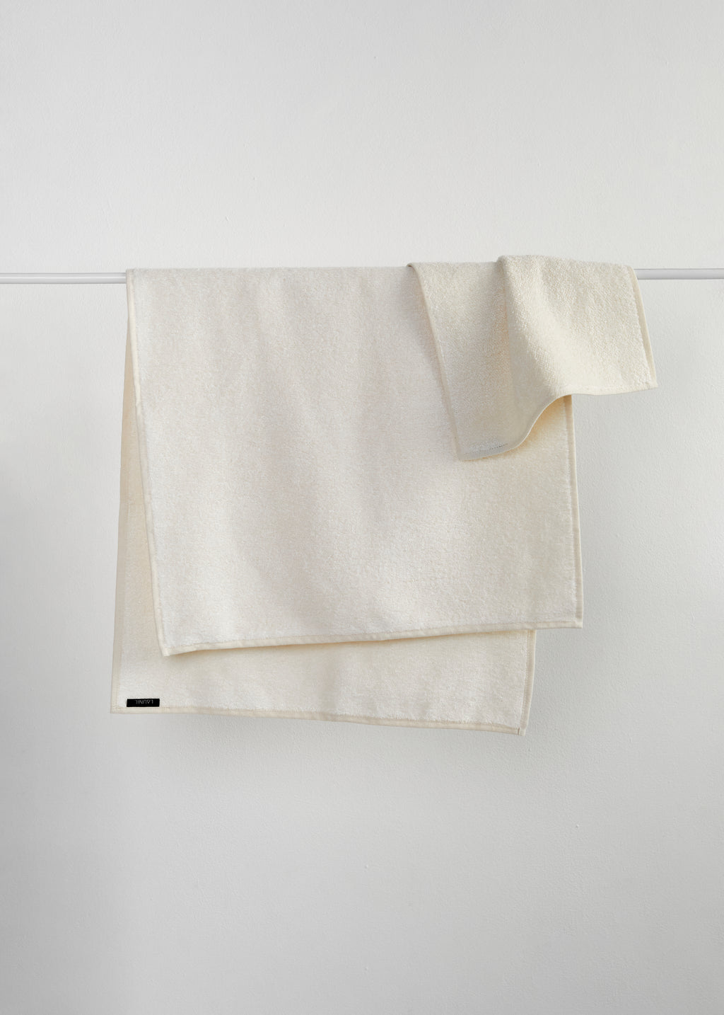 A cream-colored cotton towel draped over a thin white horizontal bar against a light gray wall.
