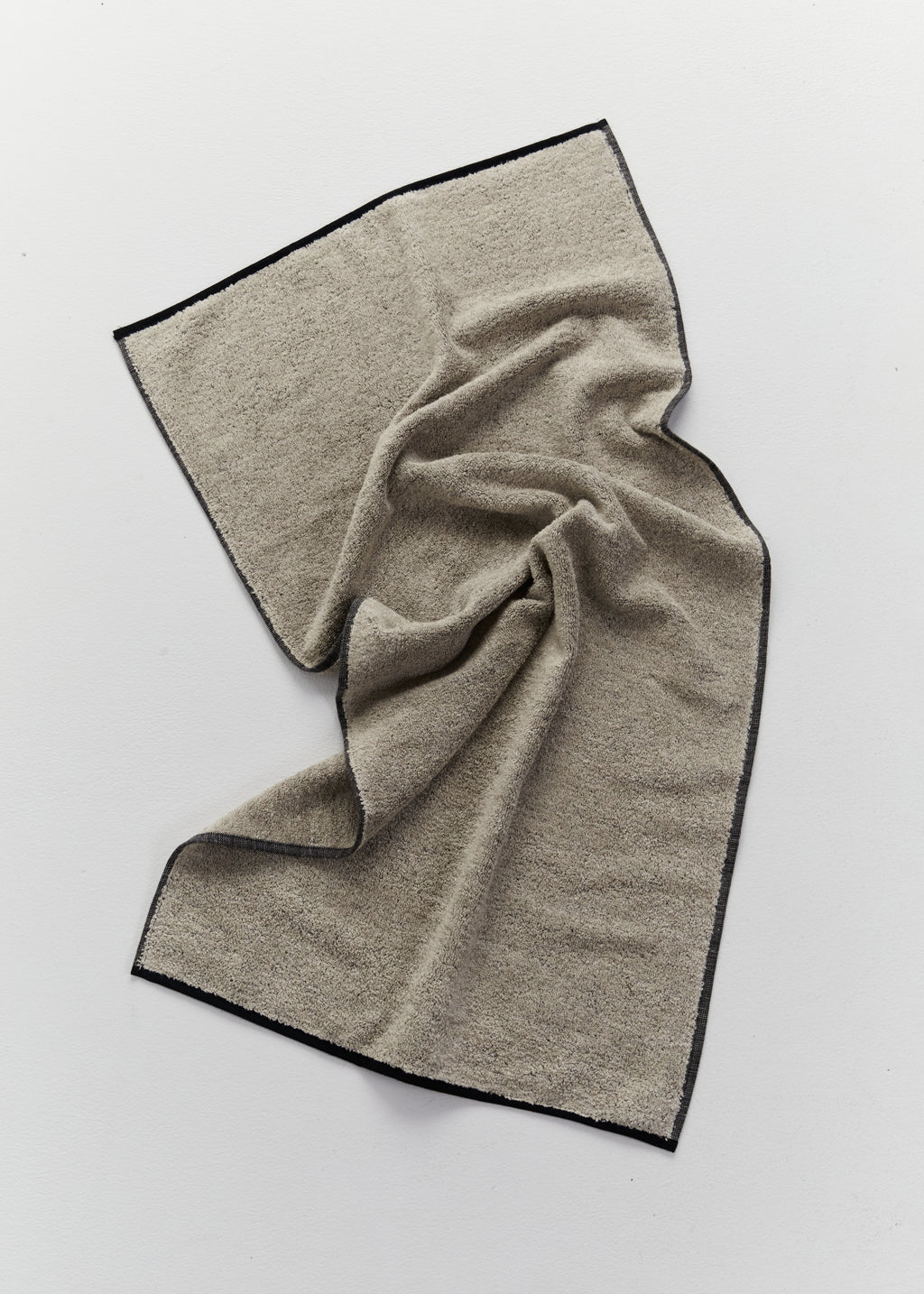 A textured beige towel with black stitched borders, draped in soft folds on a light gray background.