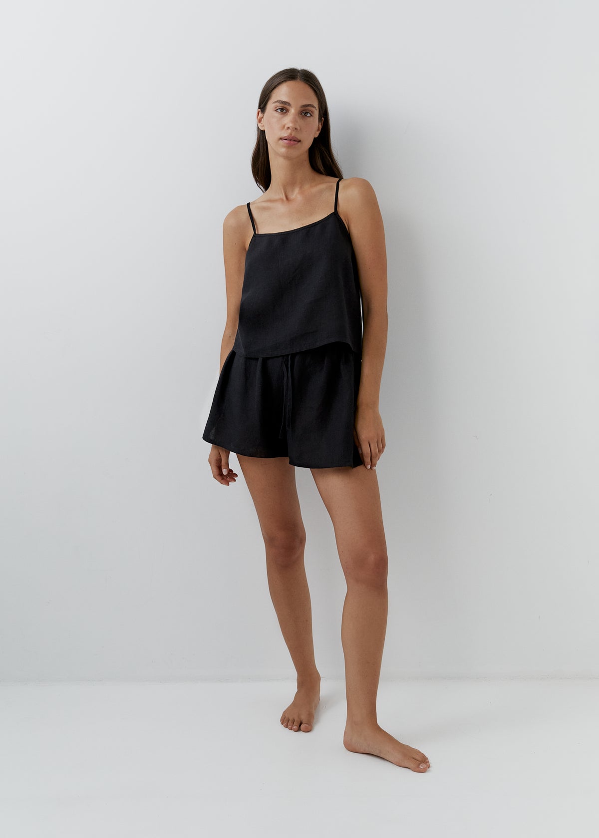 Woman wearing a black linen camisole set with matching shorts.