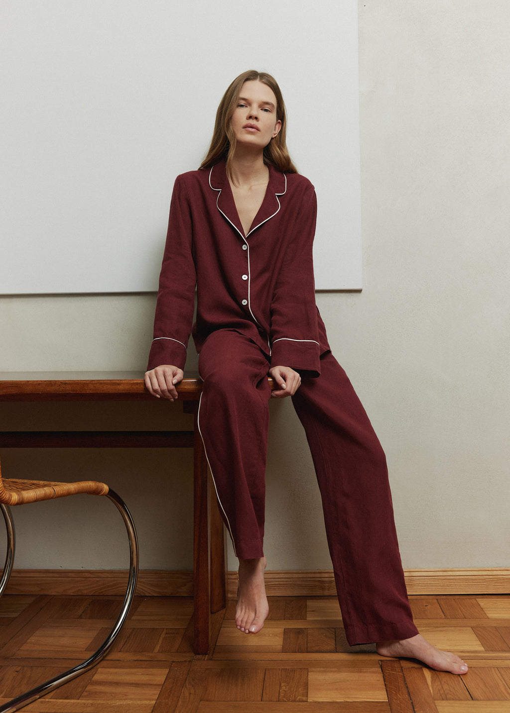 Woman wearing a burgundy linen pajama set with contrasting white piping. 
