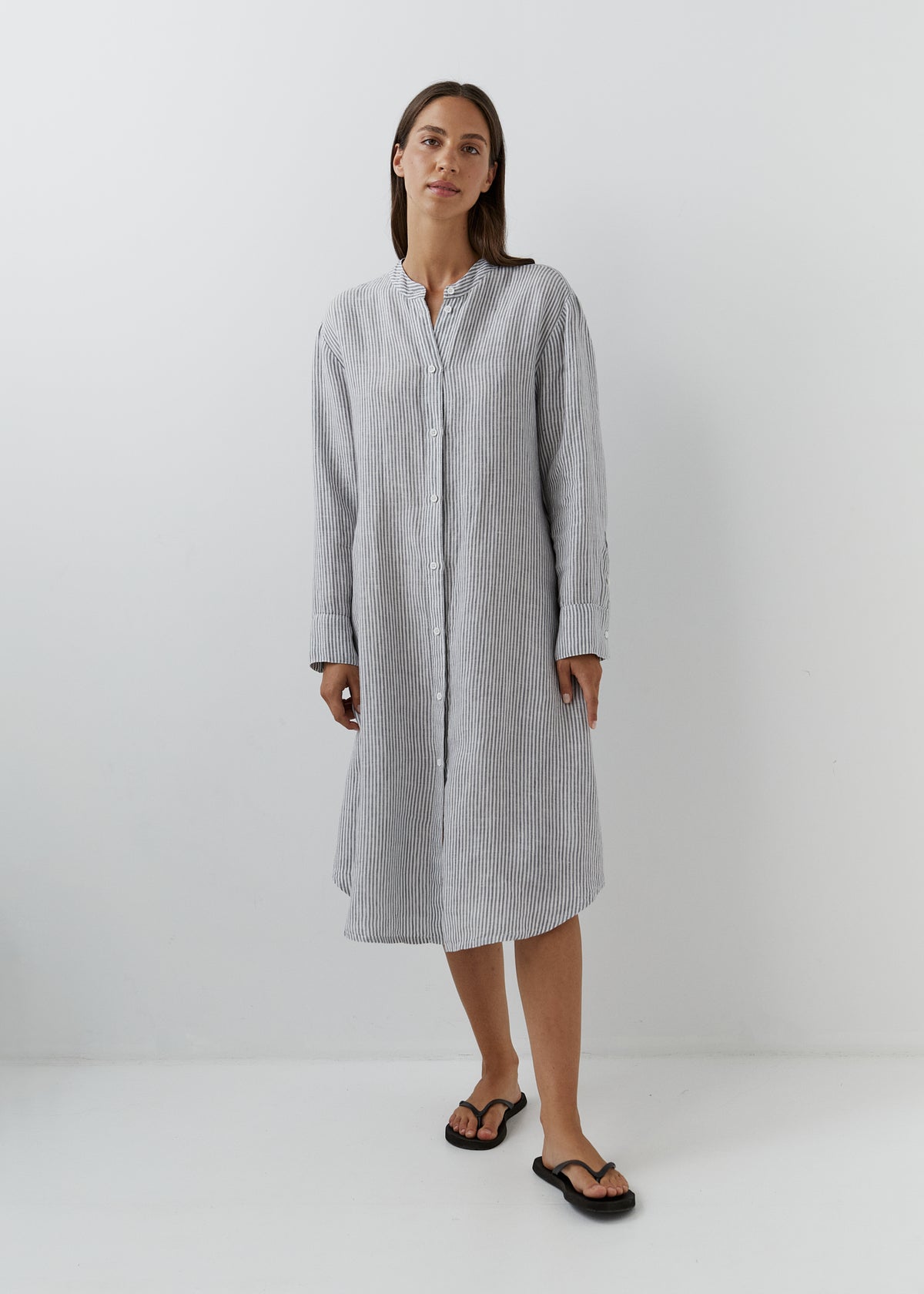 Woman wearing a grey and white striped linen midi shirt dress with long sleeves, button front and relaxed fit.