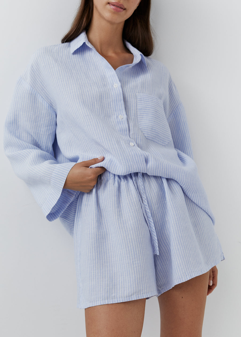 Woman wearing a fine blue striped linen short pajama set with a long-sleeved shirt and matching shorts.