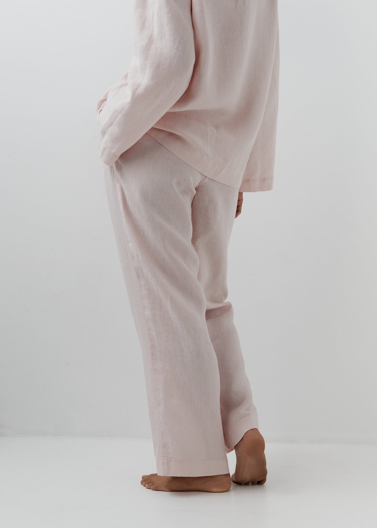 A person wearing a light blush pink linen loungwear set, shown from the back in a studio setting with a white background.