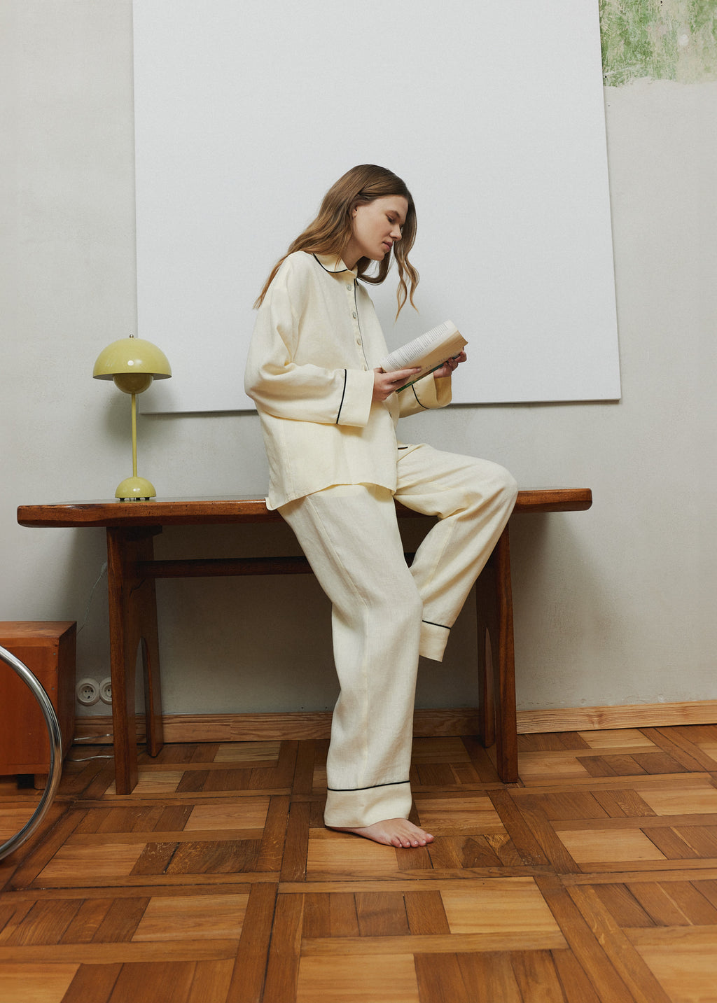 Woman reading at home in a pastel yellow linen pyjama set with black piping, relaxed linen loungewear for slow mornings.