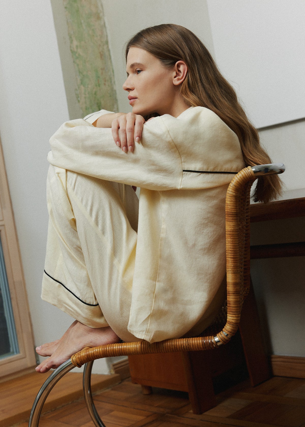 Women's pastel yellow linen loungewear set with thin black piping, relaxed sleepwear worn at home, seated view.