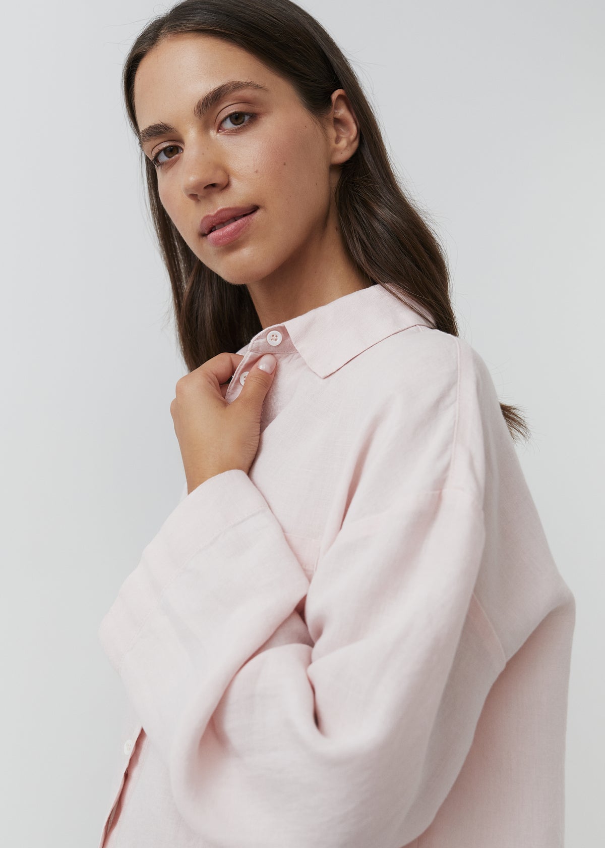 Close-up of a woman wearing a soft rose linen pyjama shirt with a classic collar and button front.