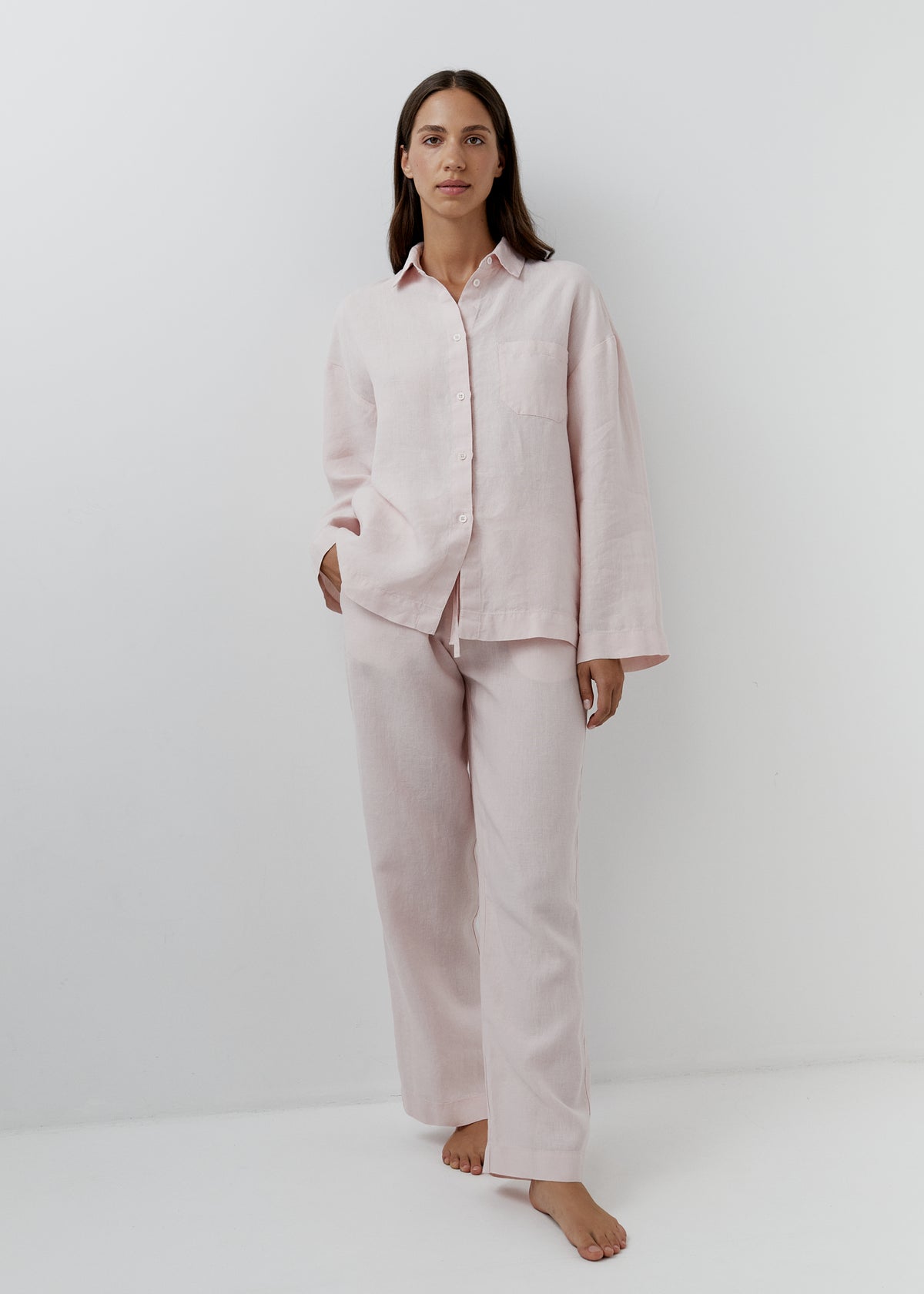 Woman wearing a rose pink linen pajama set with a long-sleeved shirt and matching trousers.
