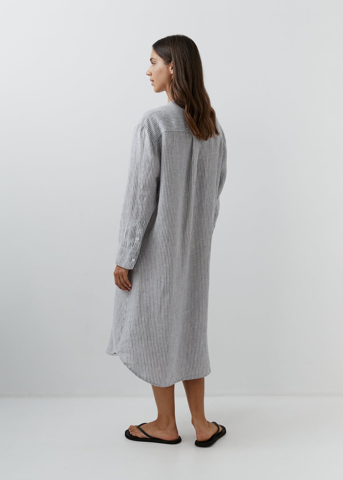 Woman wearing a grey and white striped linen midi shirt dress with long sleeves and a relaxed fit, shown from the back.