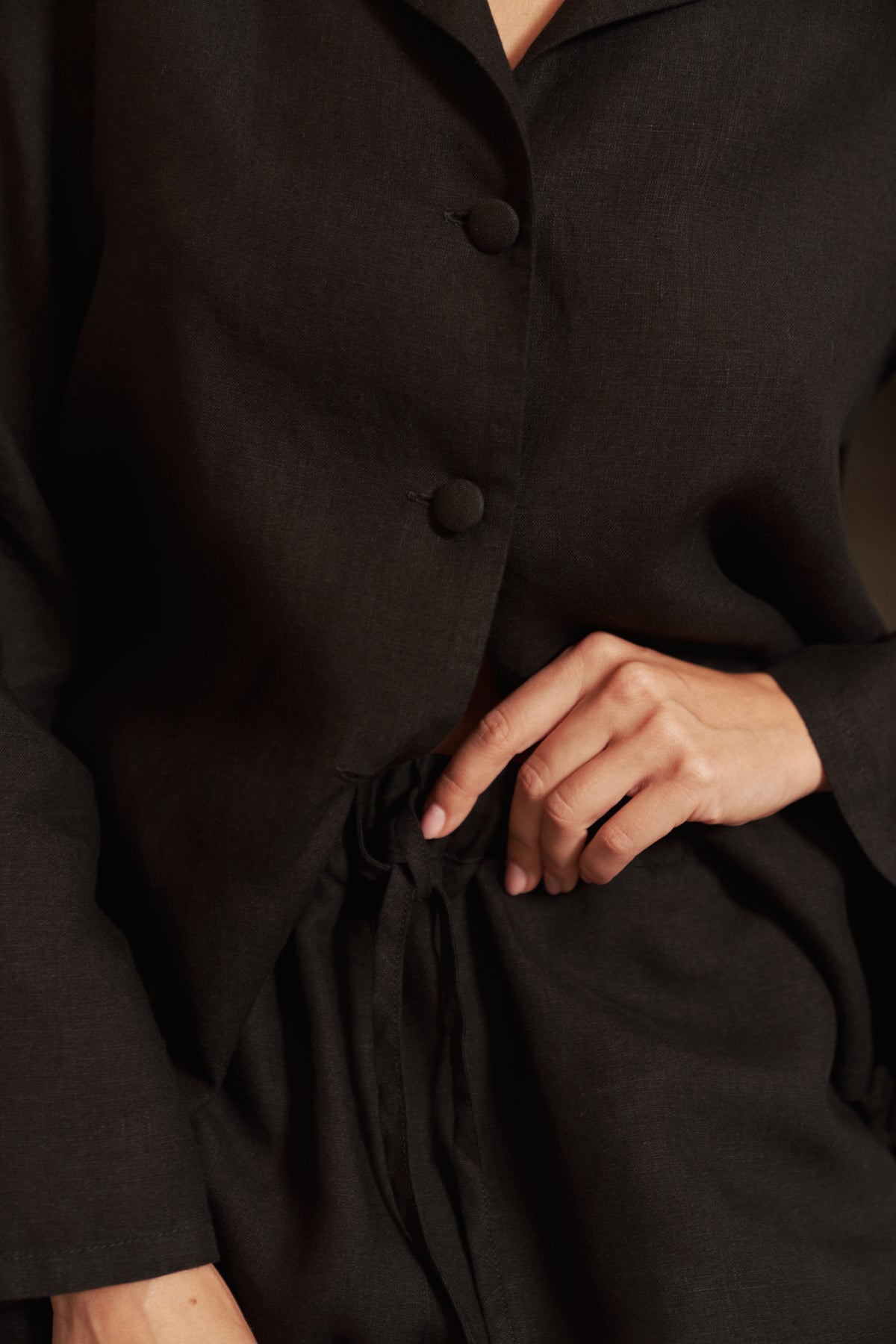 A close-up of a woman wearing a black linen pyjama set, showing fabric-covered buttons and drawstring waist pants.