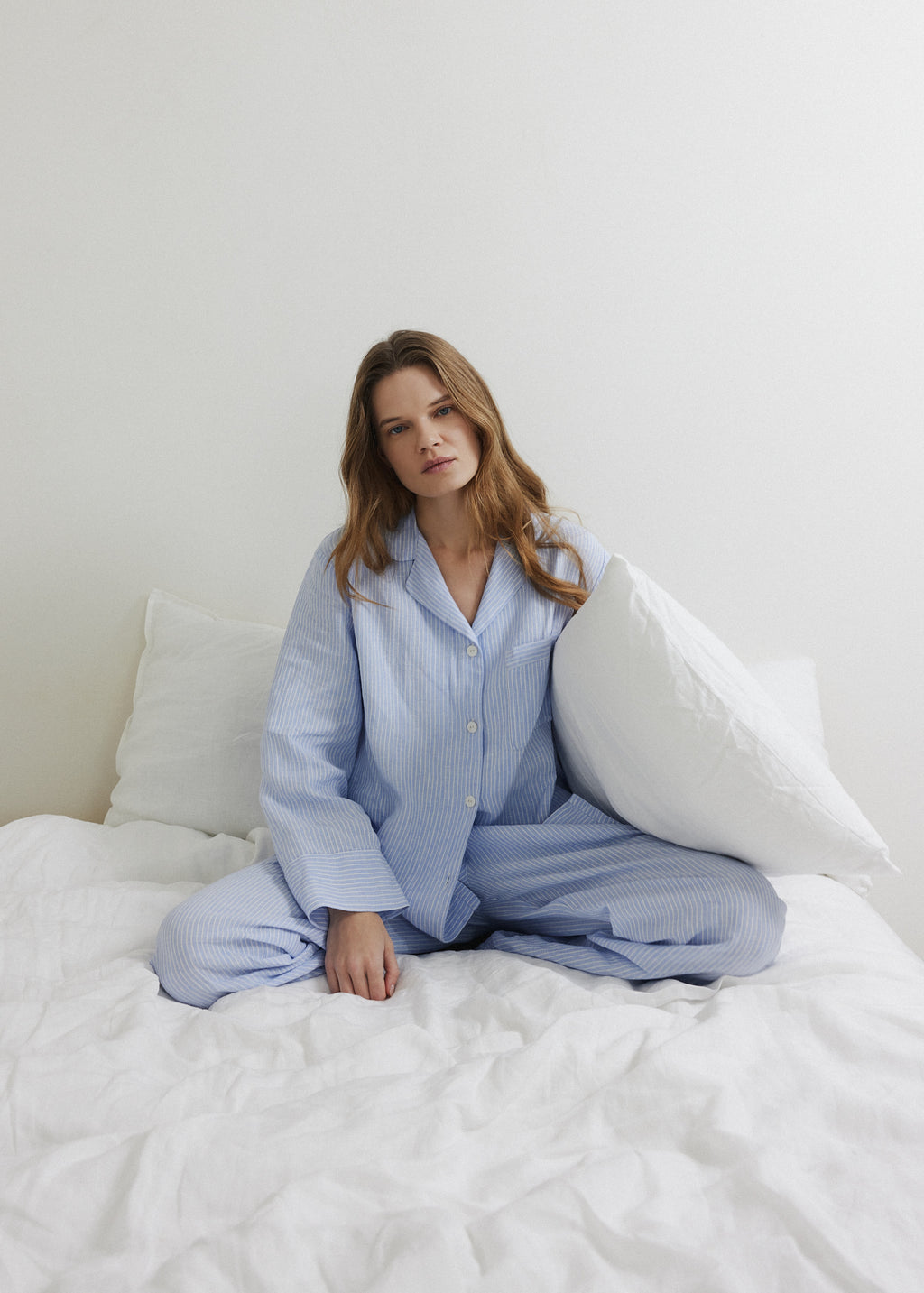 Woman relaxing in a blue and white striped linen pyjama set on linen bedding.