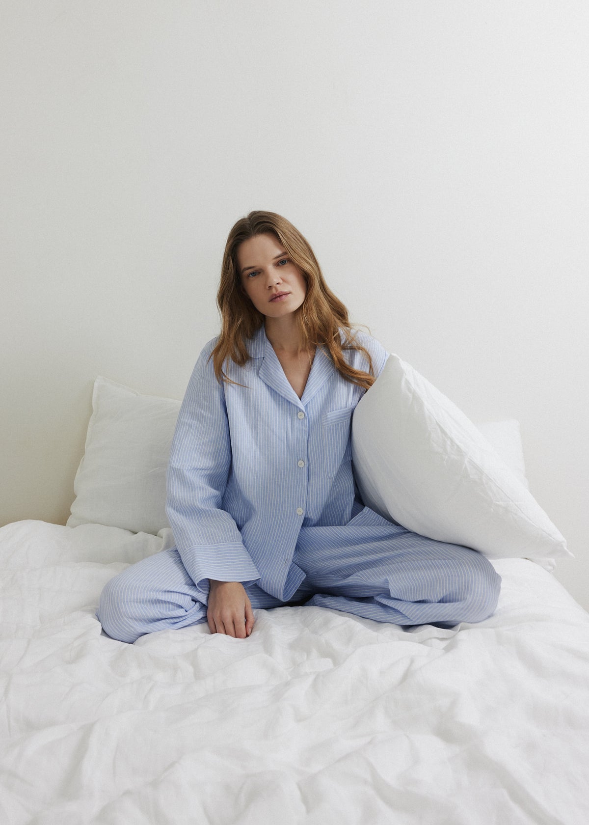 Woman relaxing in a blue and white striped linen pyjama set on linen bedding.