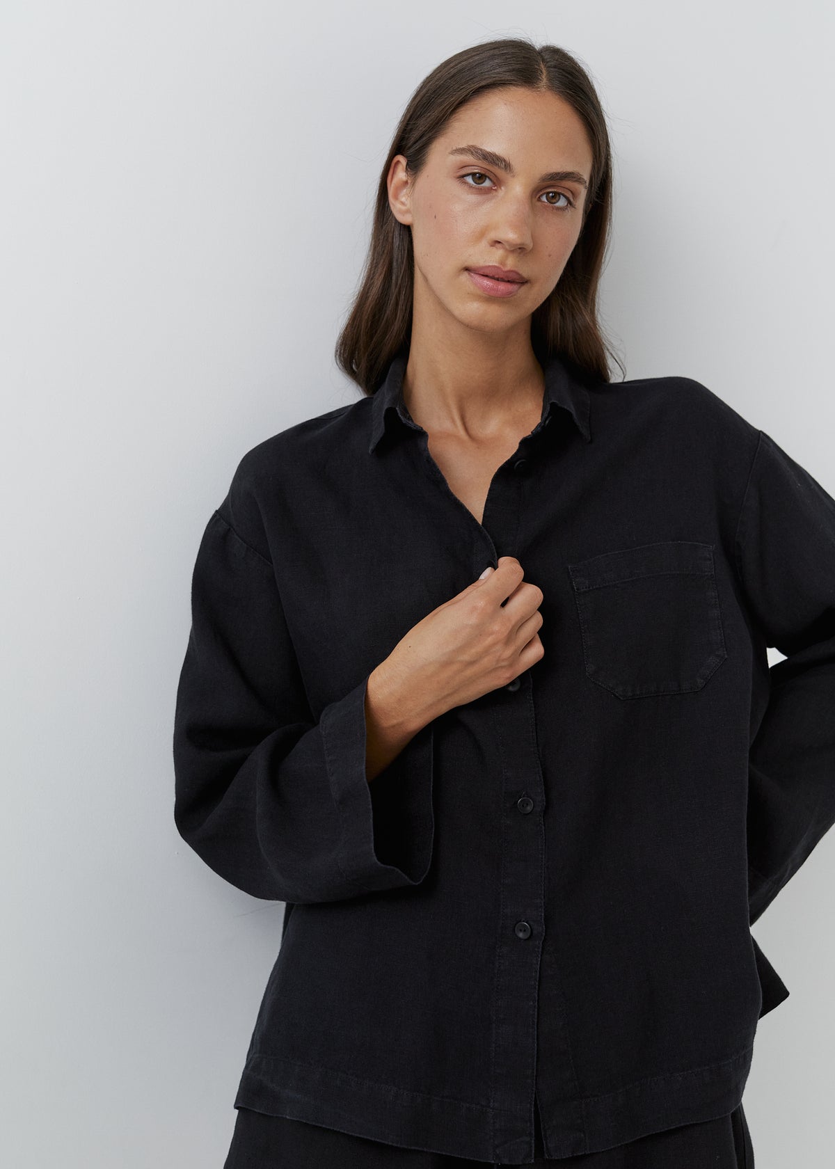 Woman wearing a relaxed black linen long-sleeve button-down shirt with a chest pocket.