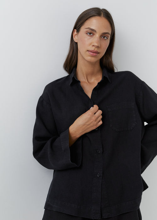 Woman wearing a relaxed black linen long-sleeve button-down shirt with a chest pocket.