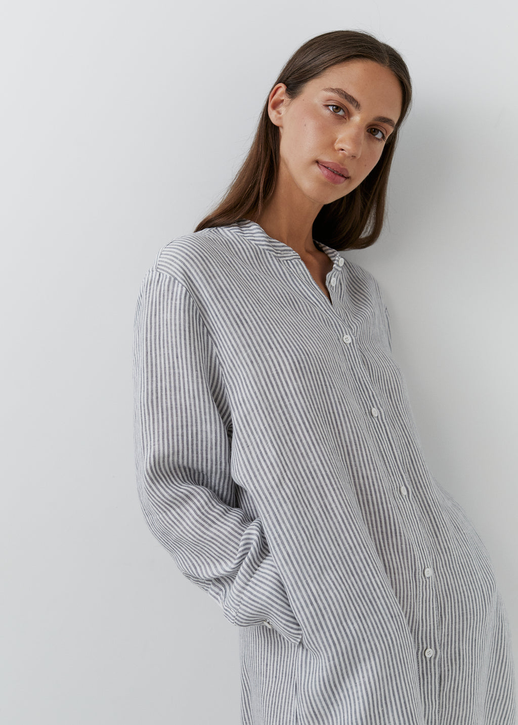 Close-up of a woman wearing a grey and white striped linen midi shirt dress with long sleeves and button front.