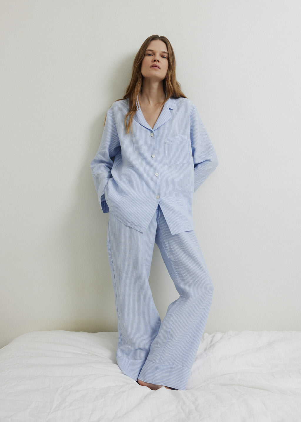 Woman wearing a blue and white striped linen pajama set with straight-leg trousers. 