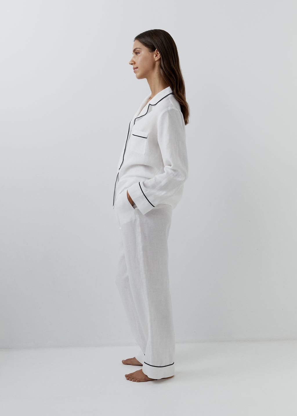 White linen nightwear set with thin black piping, button-front shirt and relaxed pants, side view.