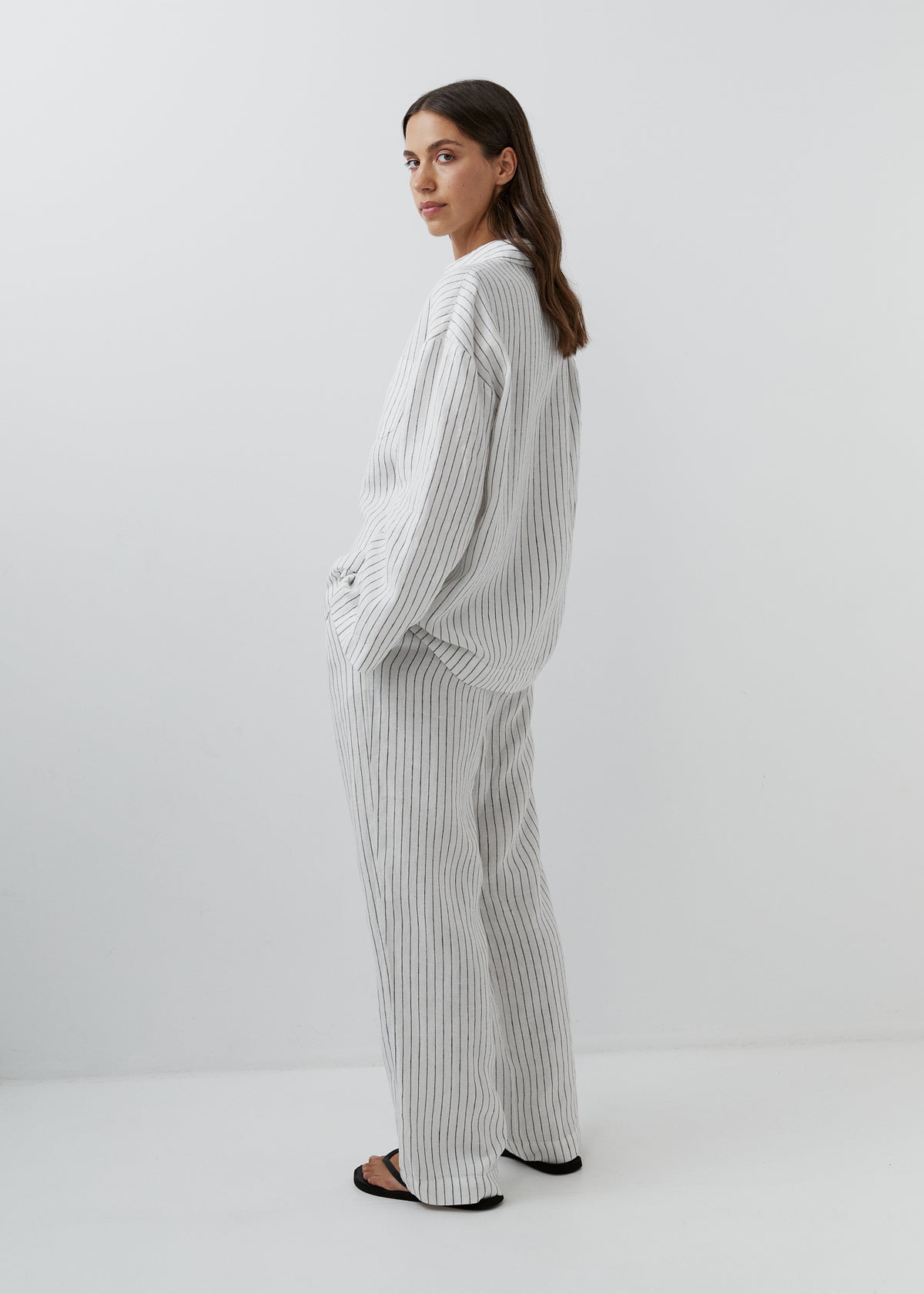 A woman modeling a matching two-piece lounge set with vertical stripes, standing in profile against a plain white studio background.