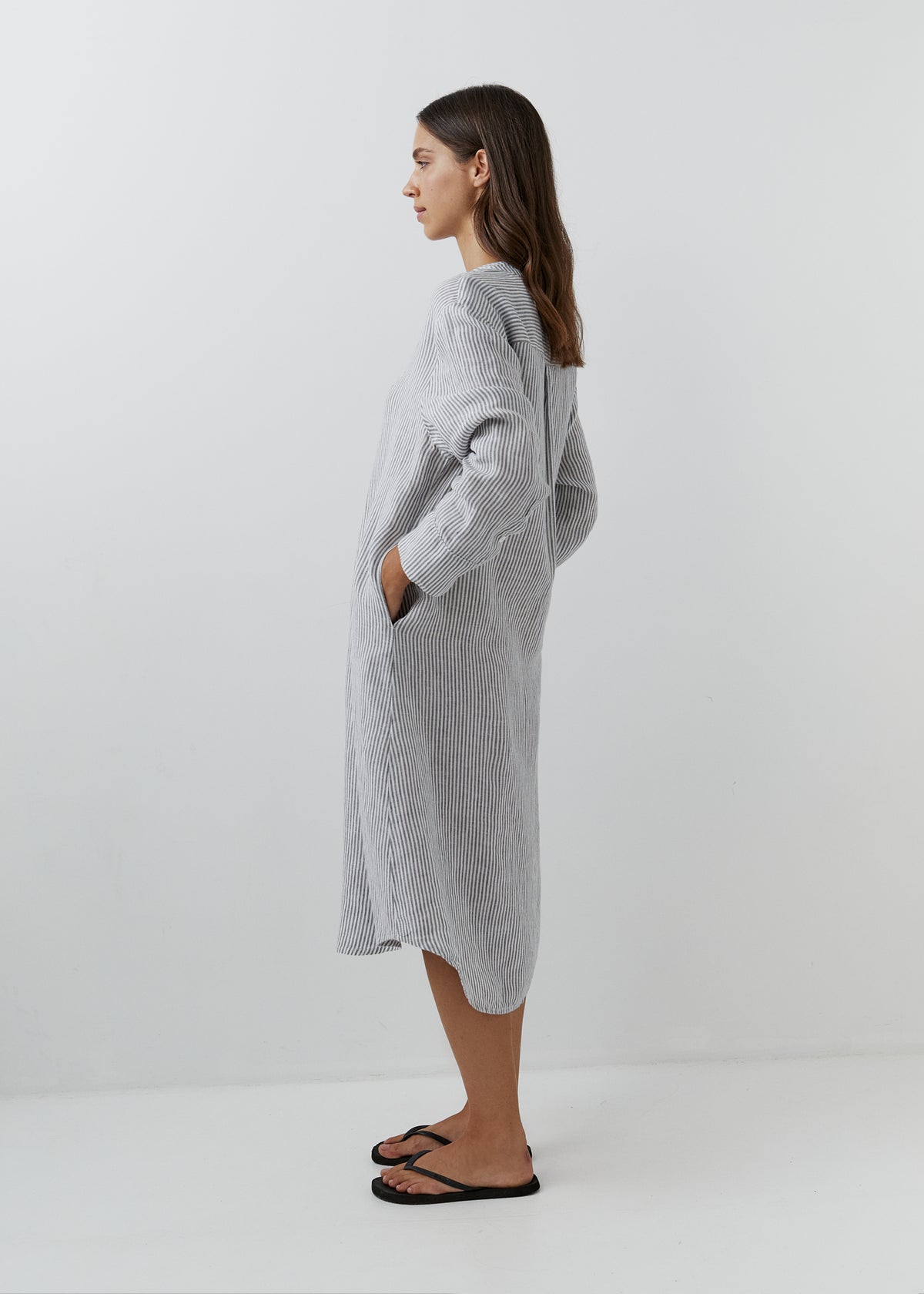 Woman wearing a grey and white striped linen midi shirt dress with long sleeves and side pockets.