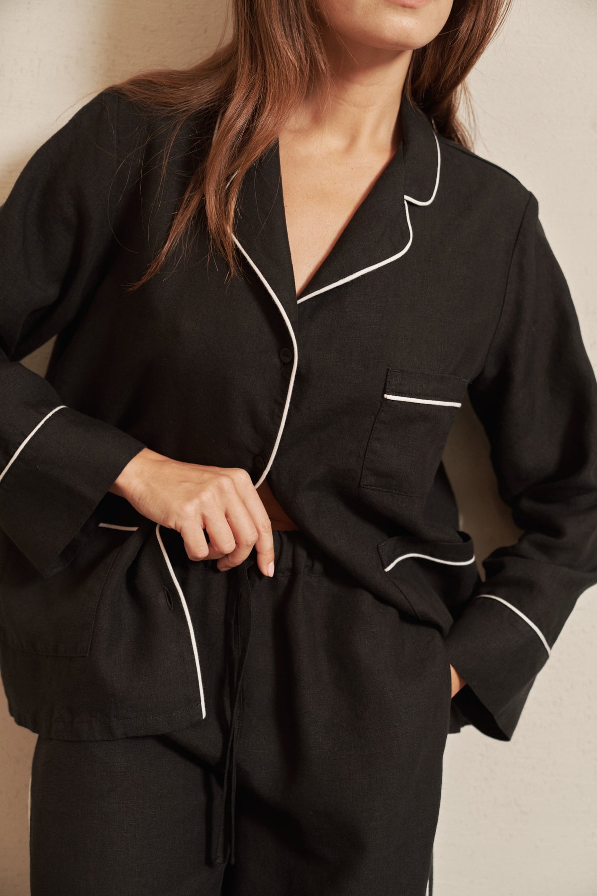 Woman wearing a black linen pyjama shirt with contrasting white piping and corozo nut buttons.