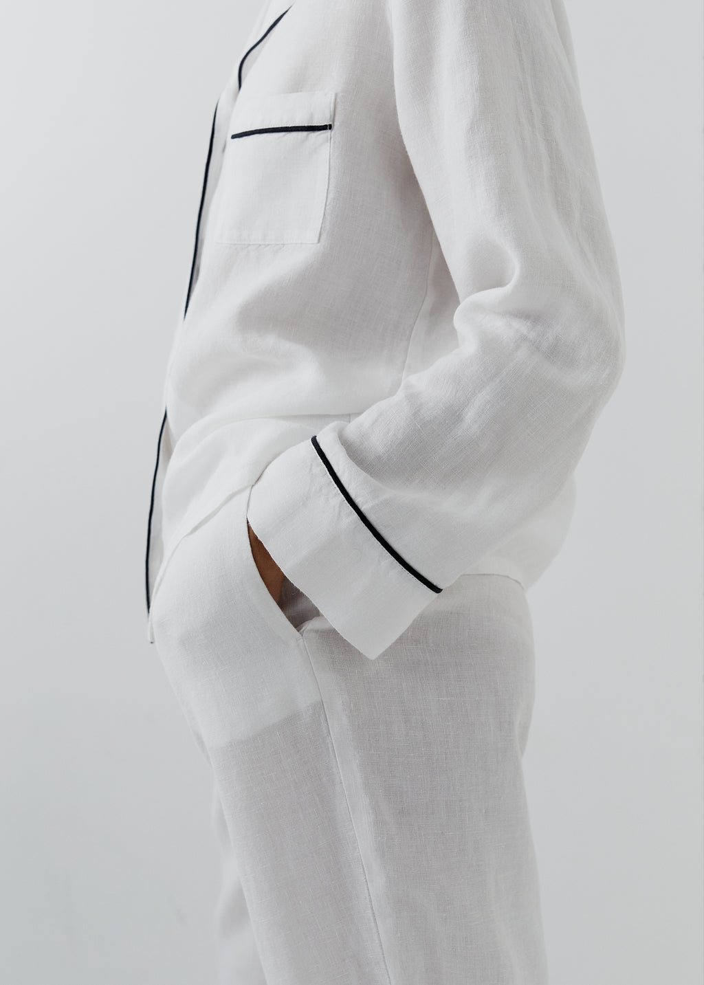 White linen pajama set with black piping trim on a model, shown in a side profile against a light gray background.
