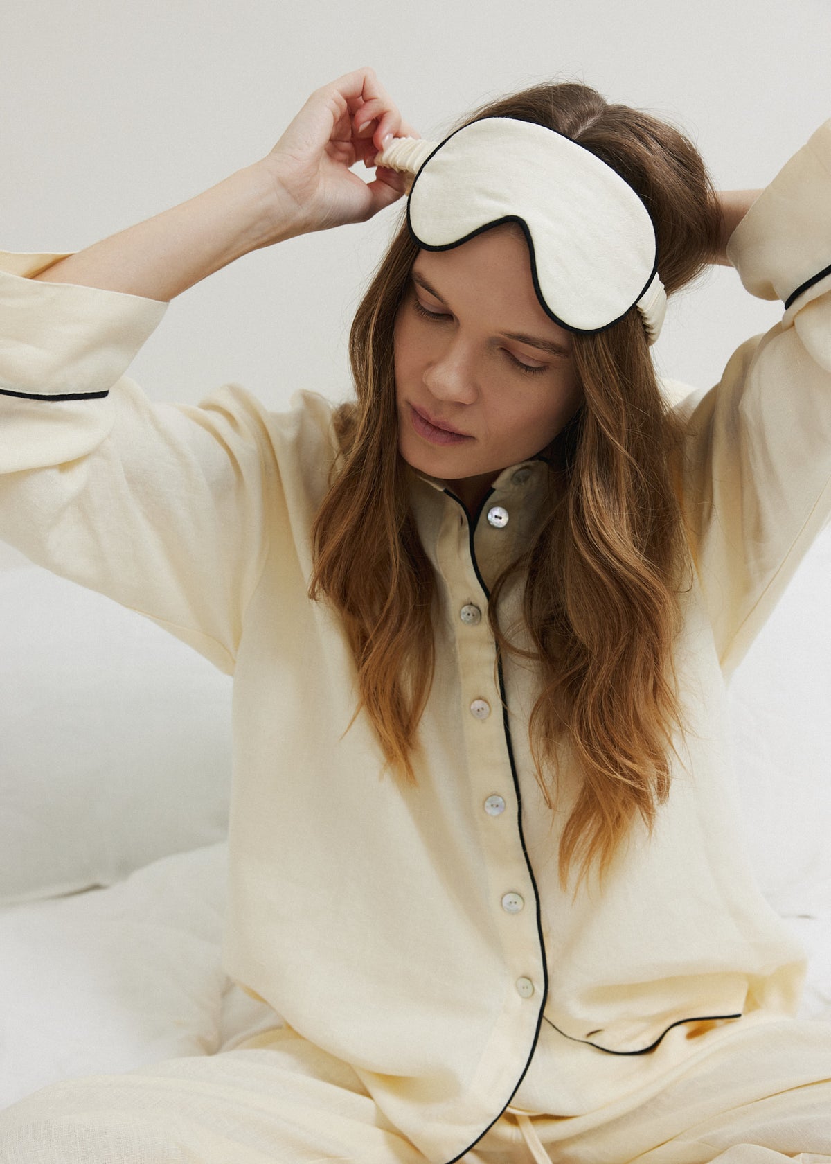 Pastel yellow linen sleepwear set with black piping and matching linen sleep mask, nightwear worn in bed.
