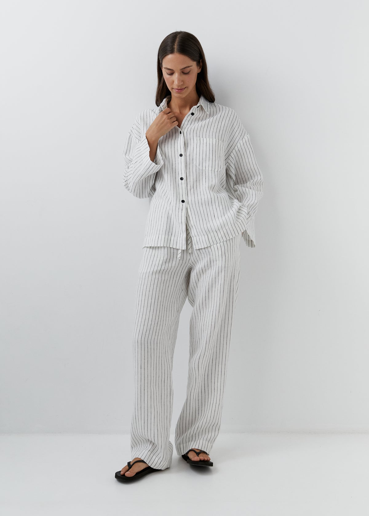 Woman wearing a fine black striped linen pajama set with a relaxed shirt and trousers.