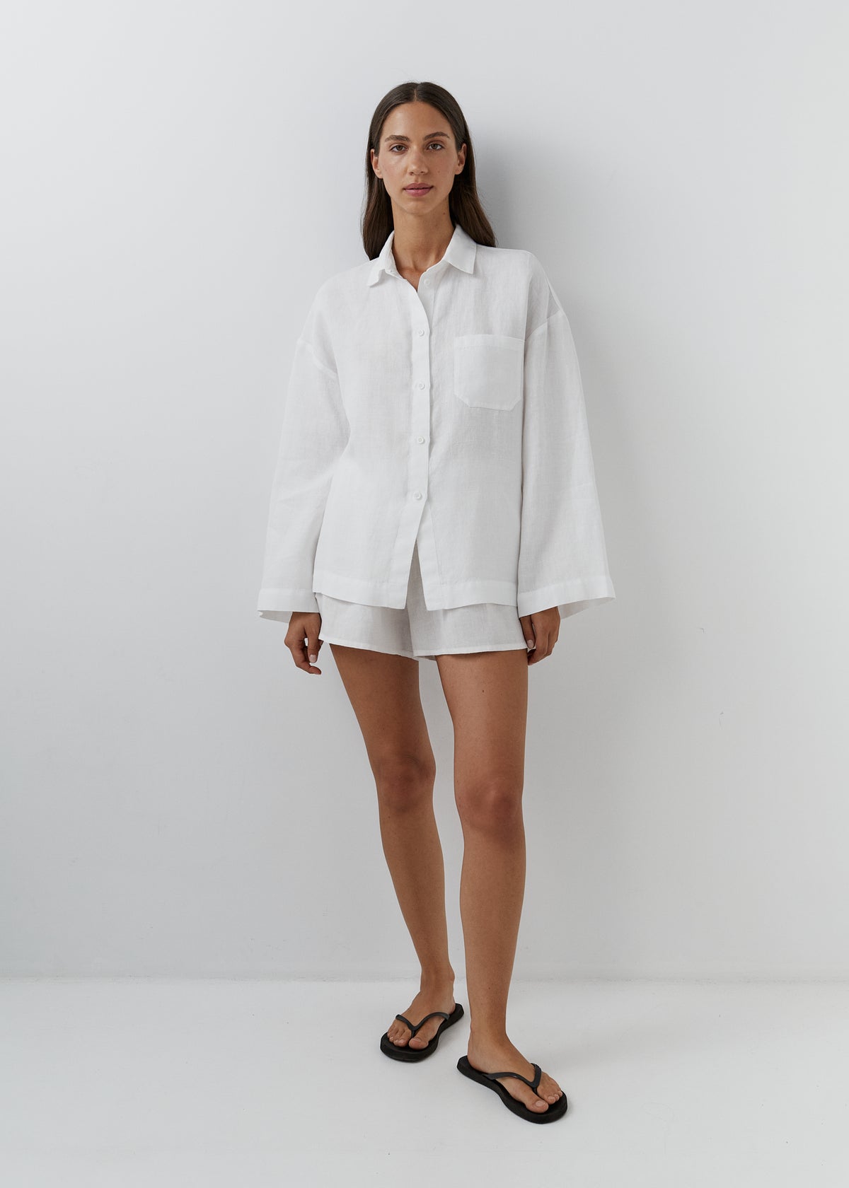 Woman wearing a relaxed white linen shirt with matching shorts. 