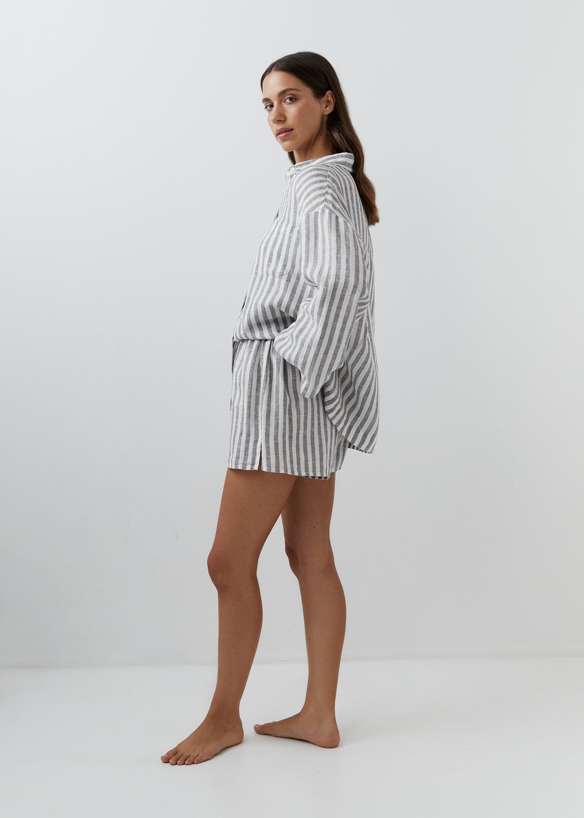 A woman modeling a matching striped lounge set consisting of a long-sleeve top and shorts, featuring vertical gray and white stripes, photographed against a plain white studio background.