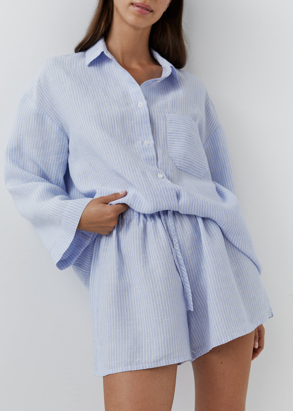 A woman wearing a light blue and white vertically striped button-up shirt and matching shorts set, photographed against a plain light gray studio background.