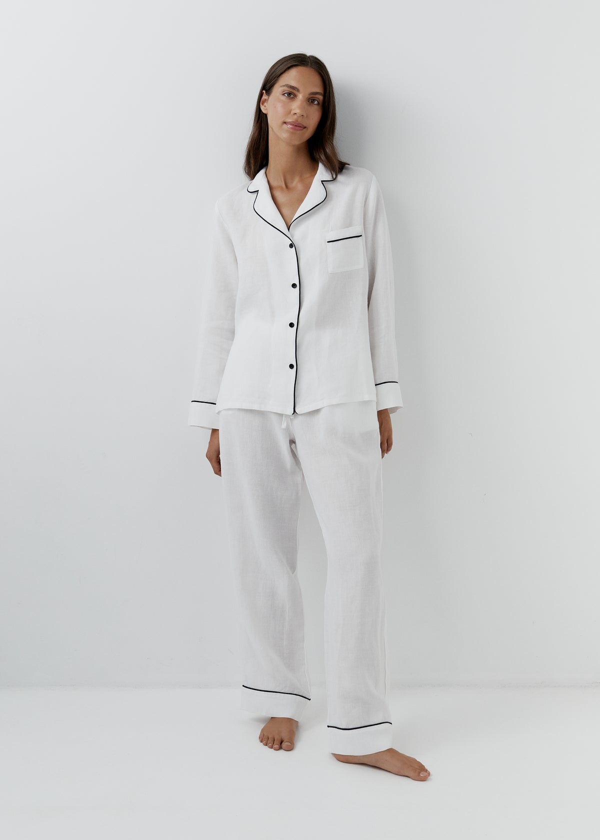 Piped Linen Pyjama Set in White, two-piece white linen pyjamas with black piping, button-up shirt and wide-leg trousers, front view. 