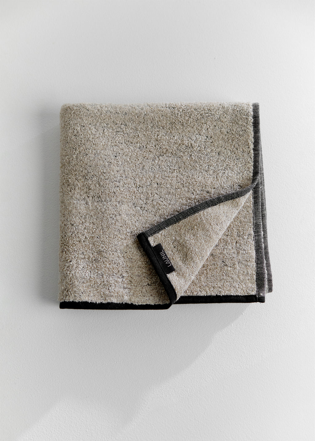 Folded sand-colored linen terry towel with dark gray edging and a LAUNIL label on a plain light background.