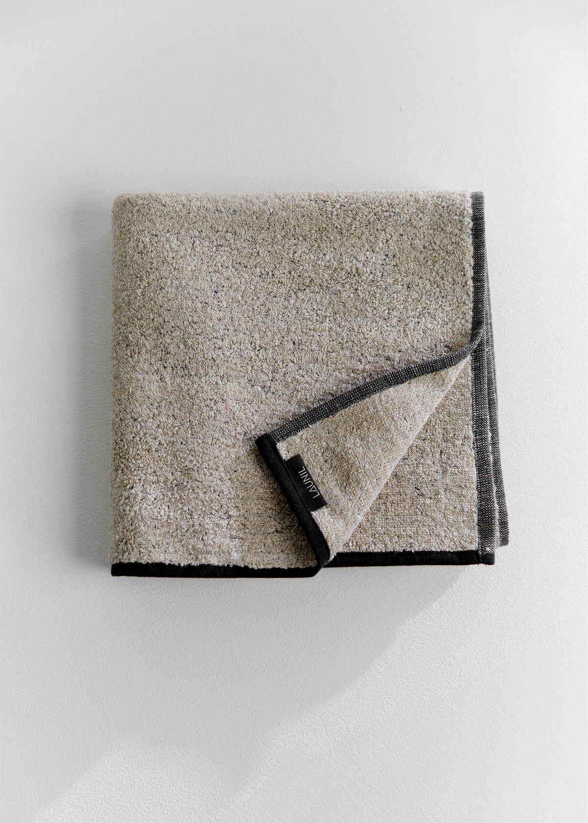 Folded sand-colored linen terry towel with dark gray edging and a LAUNIL label on a plain light background.