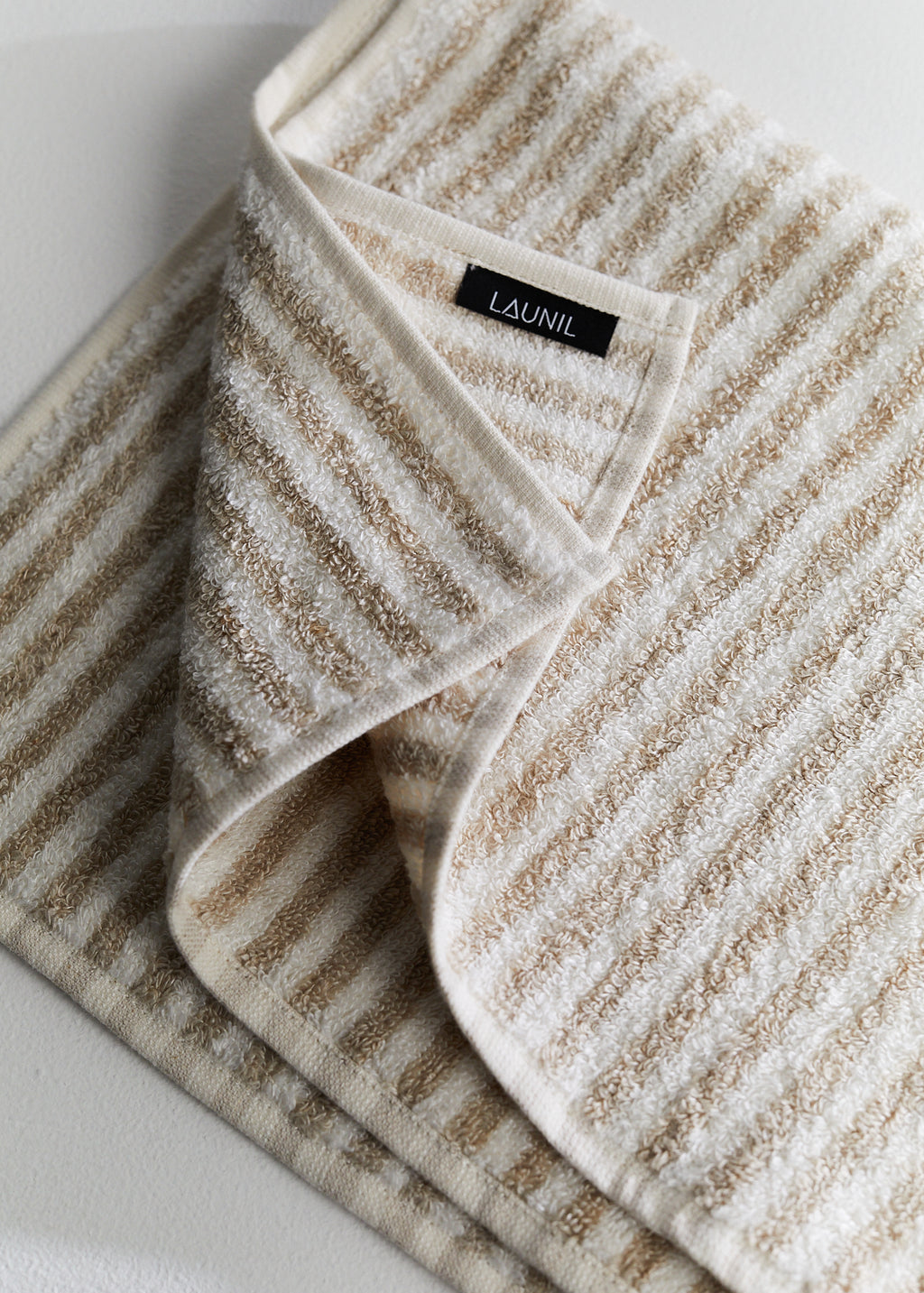A folded beige and off-white striped LAUNIL linen towel on a light neutral background.