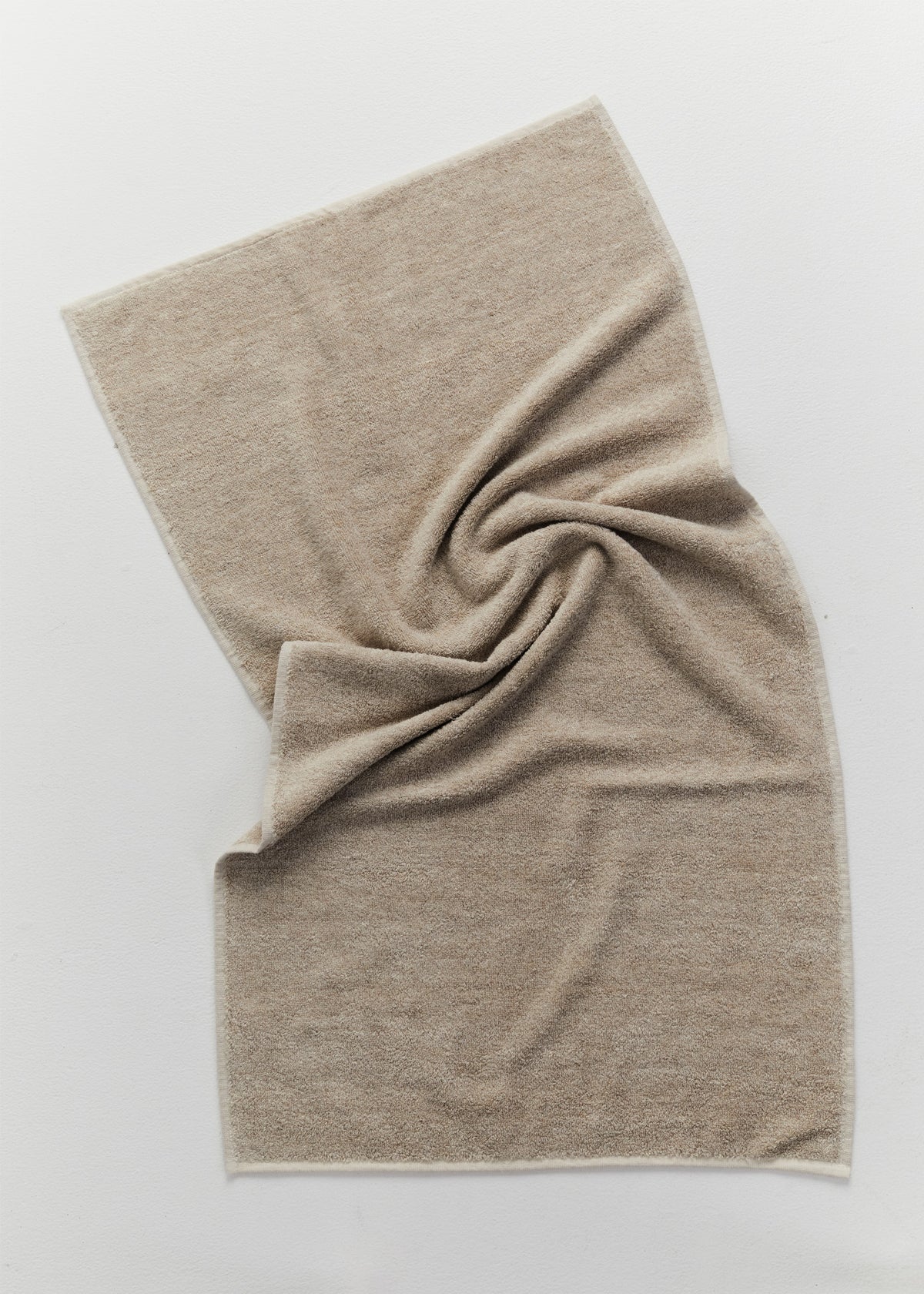 A terry beige linen cotton towel with a soft, textured weave, arranged in a gentle spiral on a clean white background.