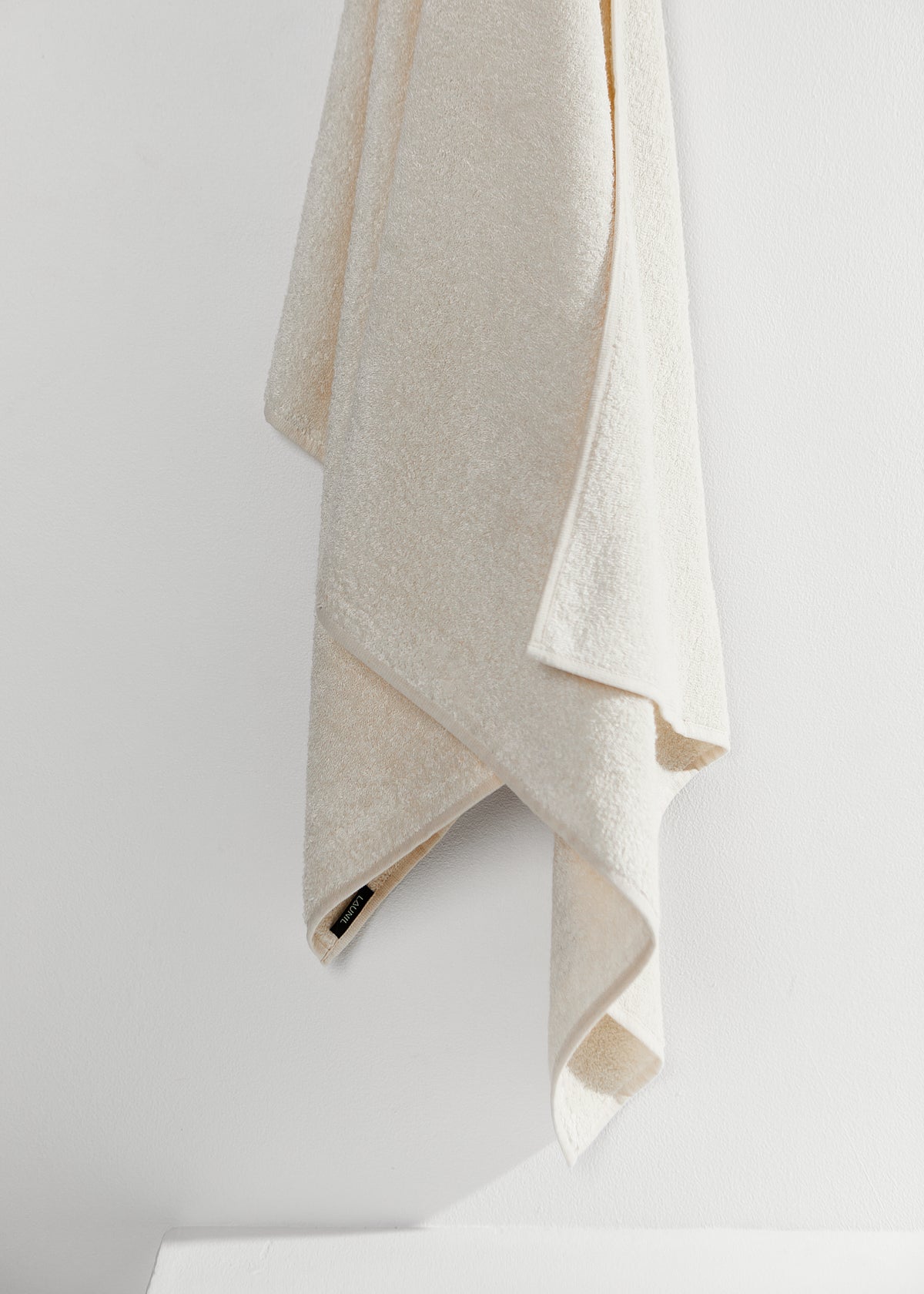 An ivory linen towel hanging from one corner against a light neutral wall.
