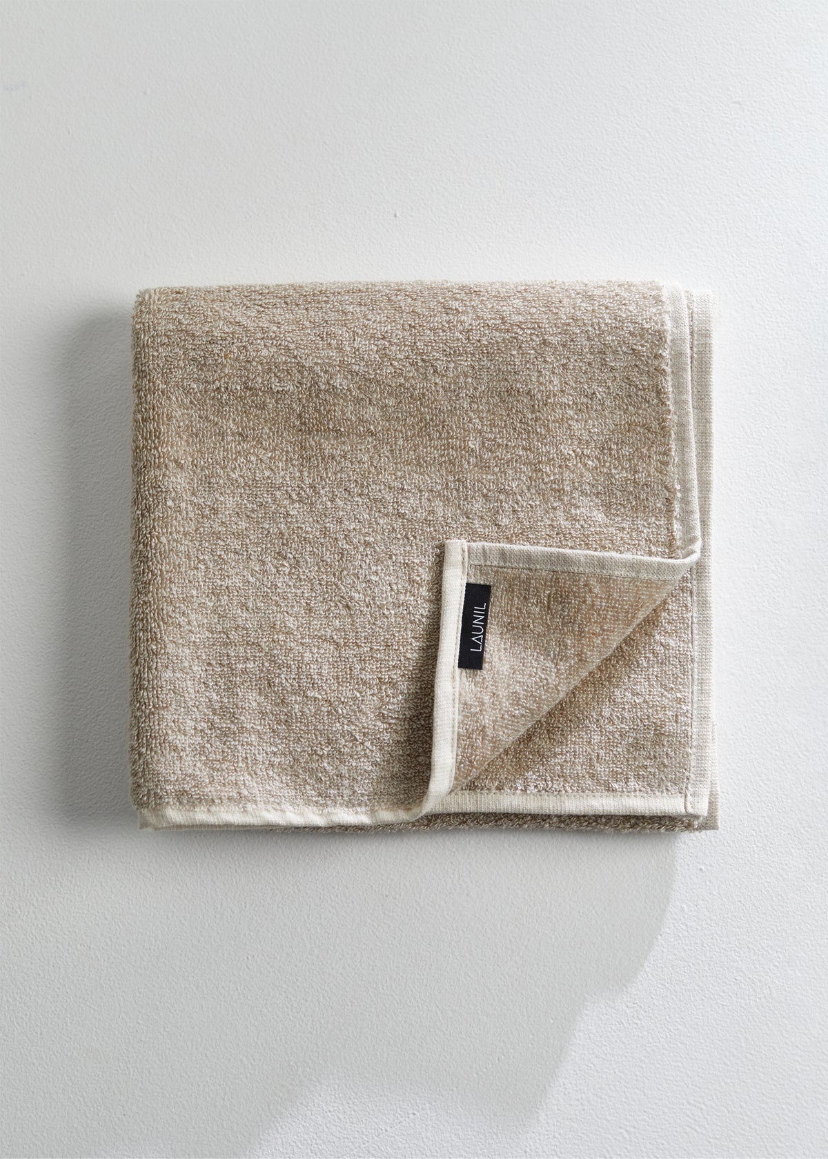 A folded beige linen and cotton towel with a textured terry surface and a small black brand tag reading "LAUNIL", displayed on a clean white background.