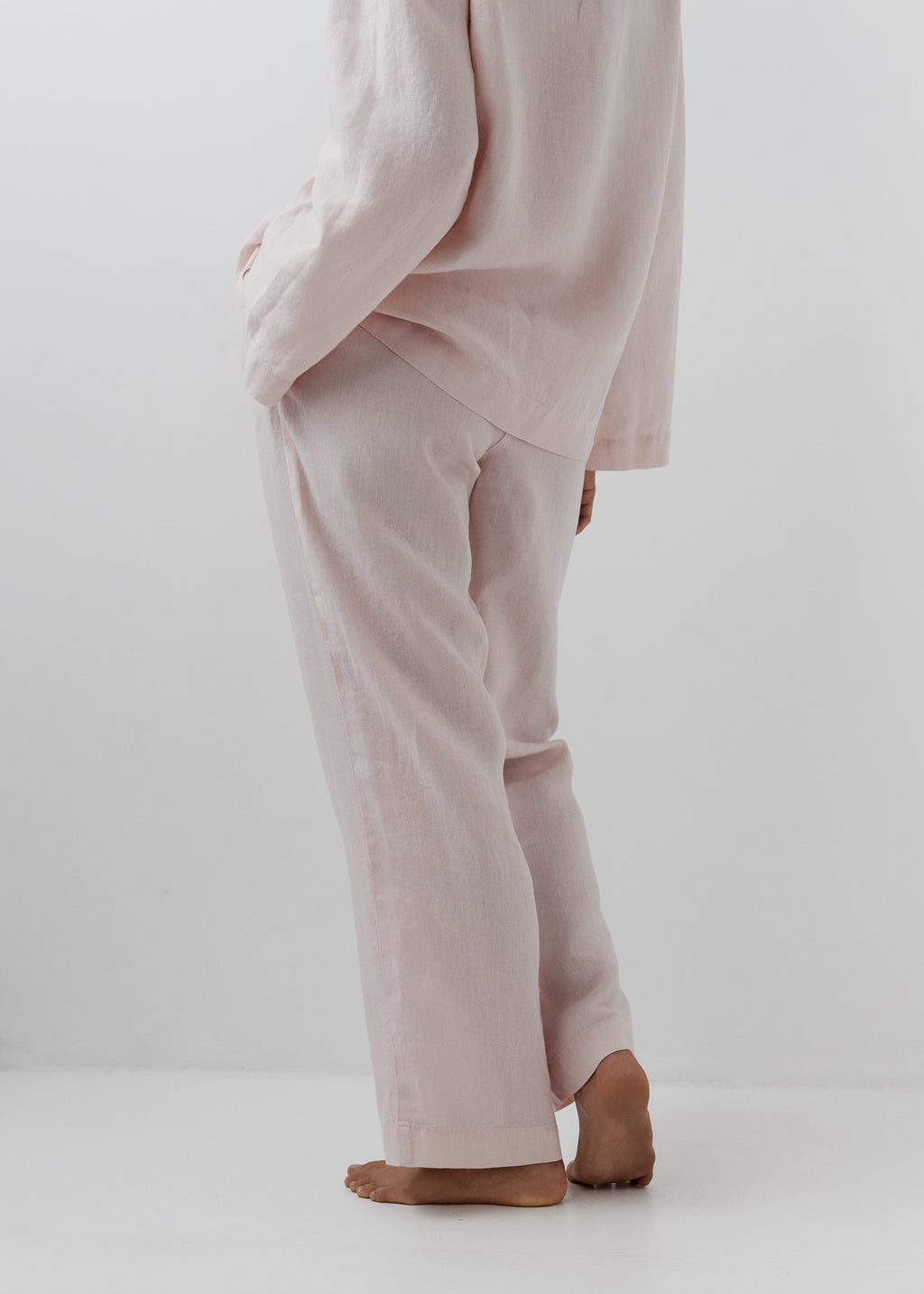 A person wearing a light blush pink linen pyjama pants, shown from the back in a studio setting with a white background.