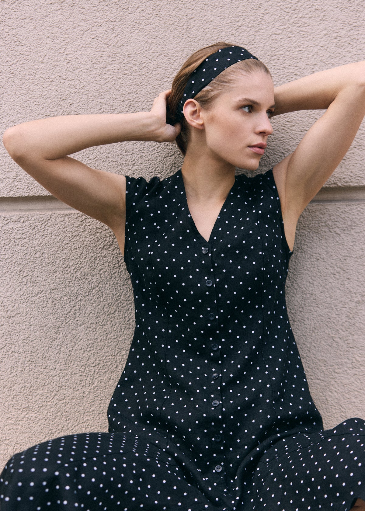 Close-up of a woman wearing a black linen polka dot dress with V-neckline, sleeveless design and front button closure, styled with a matching polka dot headband.