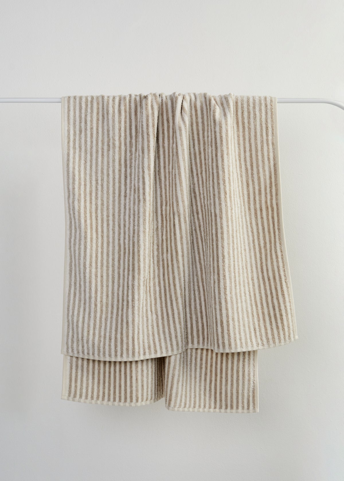 A folded beige and off-white striped linen towel hanging from a thin white rod against a light gray wall.
